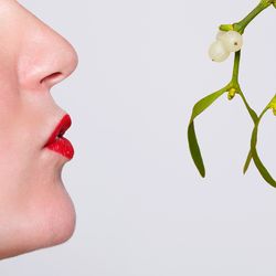 Woman kissing mistletoe on white background