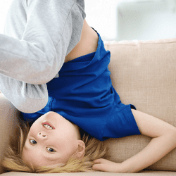 A child wearing a blue T-shirt doing a handstand on a sofa