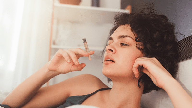 A woman smoking a cannabis cigarette in bed.