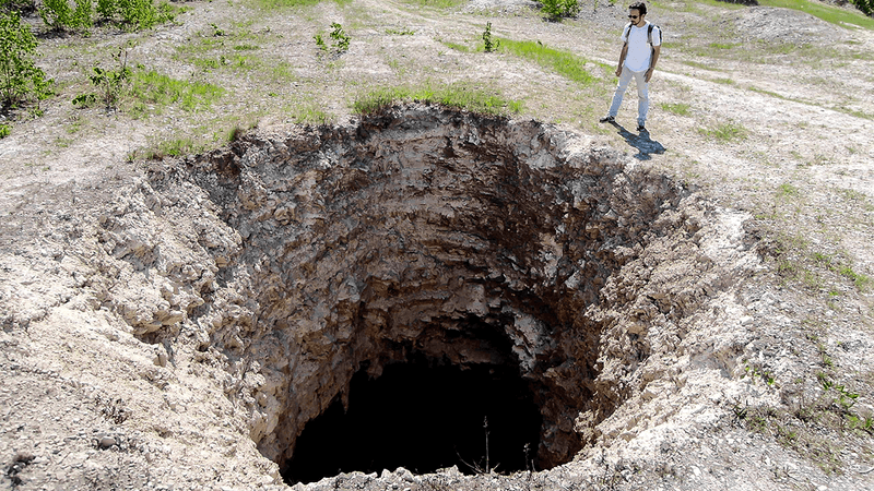 A man looking into a large sinkhole.