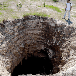 A man looking into a large sinkhole.